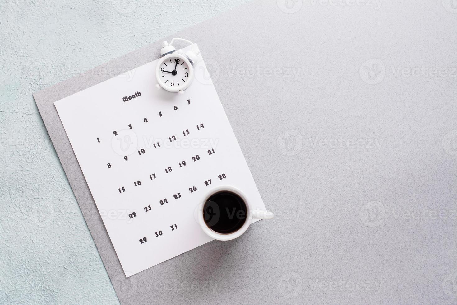 Blank sheet of monthly calendar, coffee cup and alarm clock  on textured background. Time planning and organization. Copy space photo