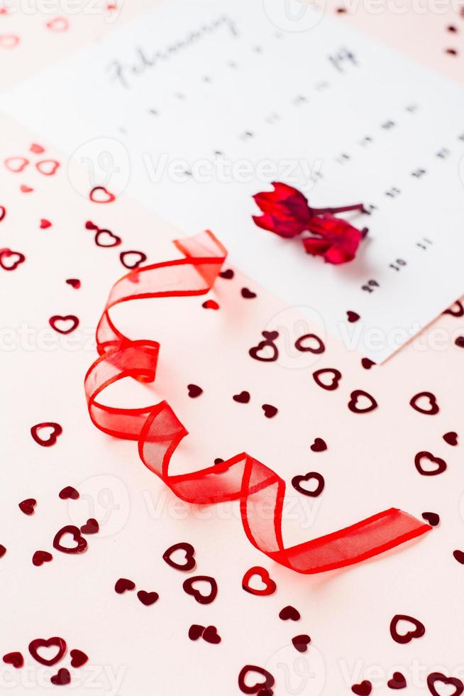 Valentine's Day. Red ribbon in the form of a spiral, dry flowers and a calendar leaf for February on a pink background with hearts. Vertical view photo