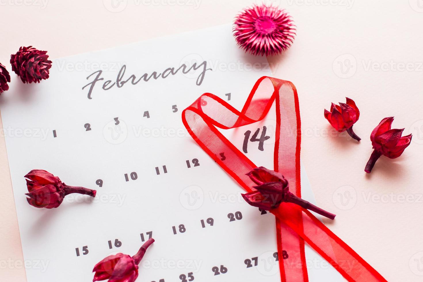 San Valentín día. un rojo en forma de corazon cinta Destacar el fecha febrero 14 en un calendario sábana y seco flores en un rosado antecedentes. de cerca foto