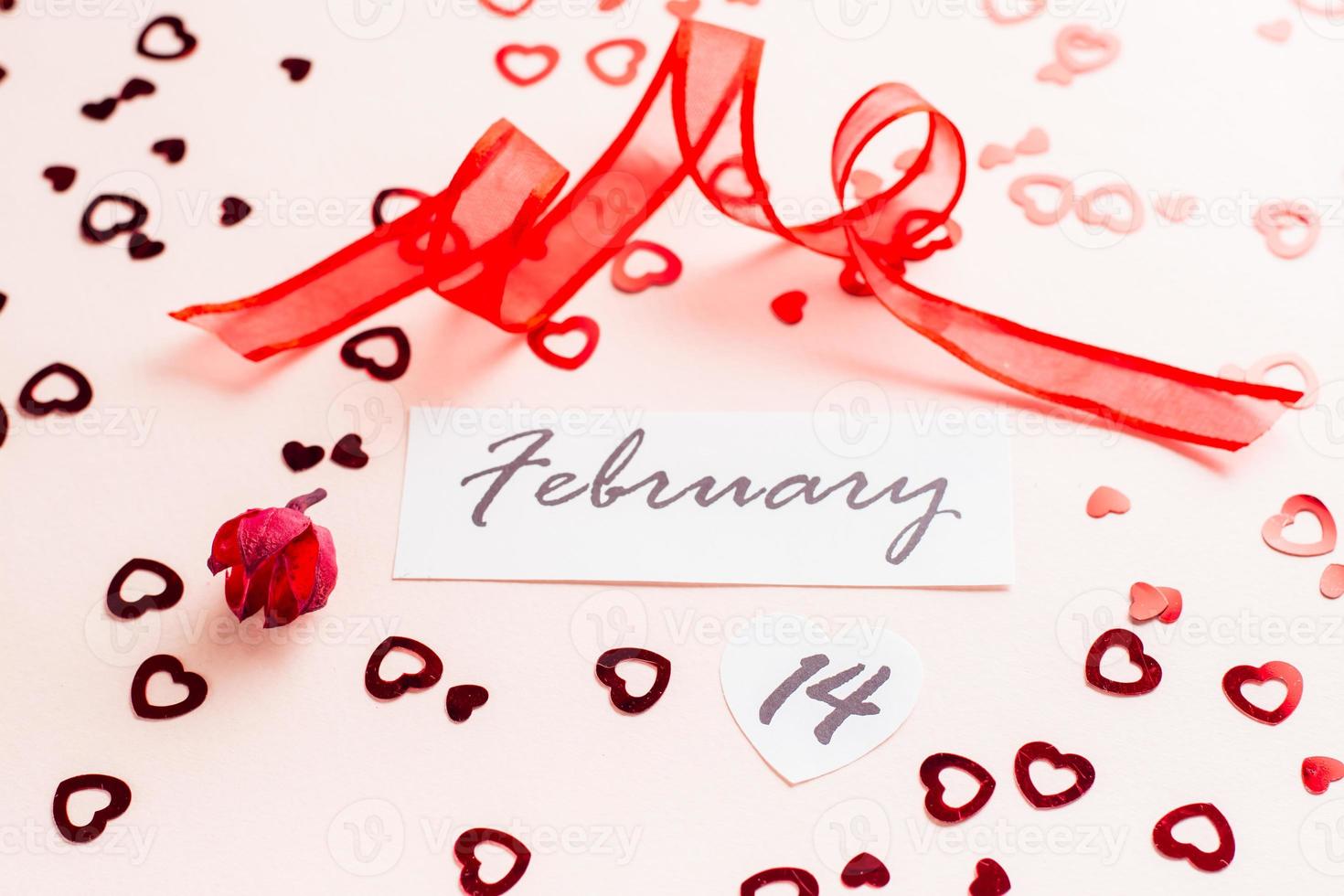 Valentine's Day. Date 14 february and red ribbon on pink heart-strewn background. Close-up photo