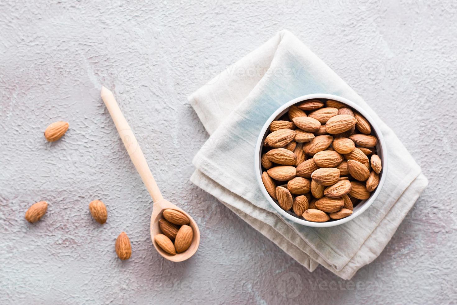 Fresh peeled almonds in a wooden spoon and in a bowl nearby on a light background. A source of vitamins and oils. Organic food. Top view photo