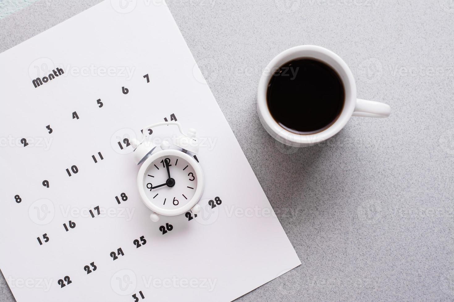 blanco sábana de mensual calendario, café taza y alarma reloj en un gris antecedentes. hora planificación y organización. Copiar espacio. de cerca foto