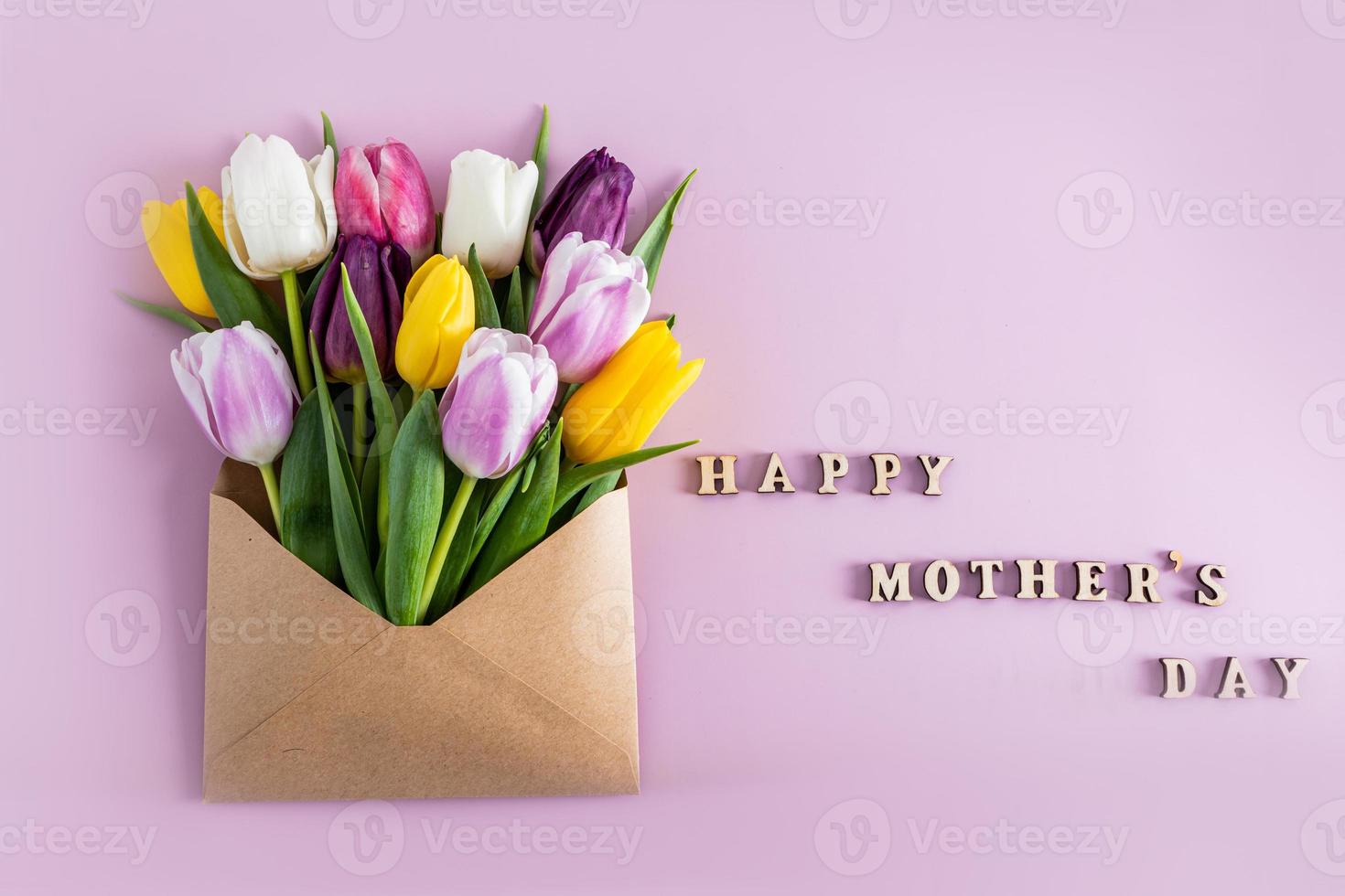 creative composition for the mother's day holiday. lots of colorful spring flowers in a craft envelope. flat lay. letters wooden happy mother's day. photo