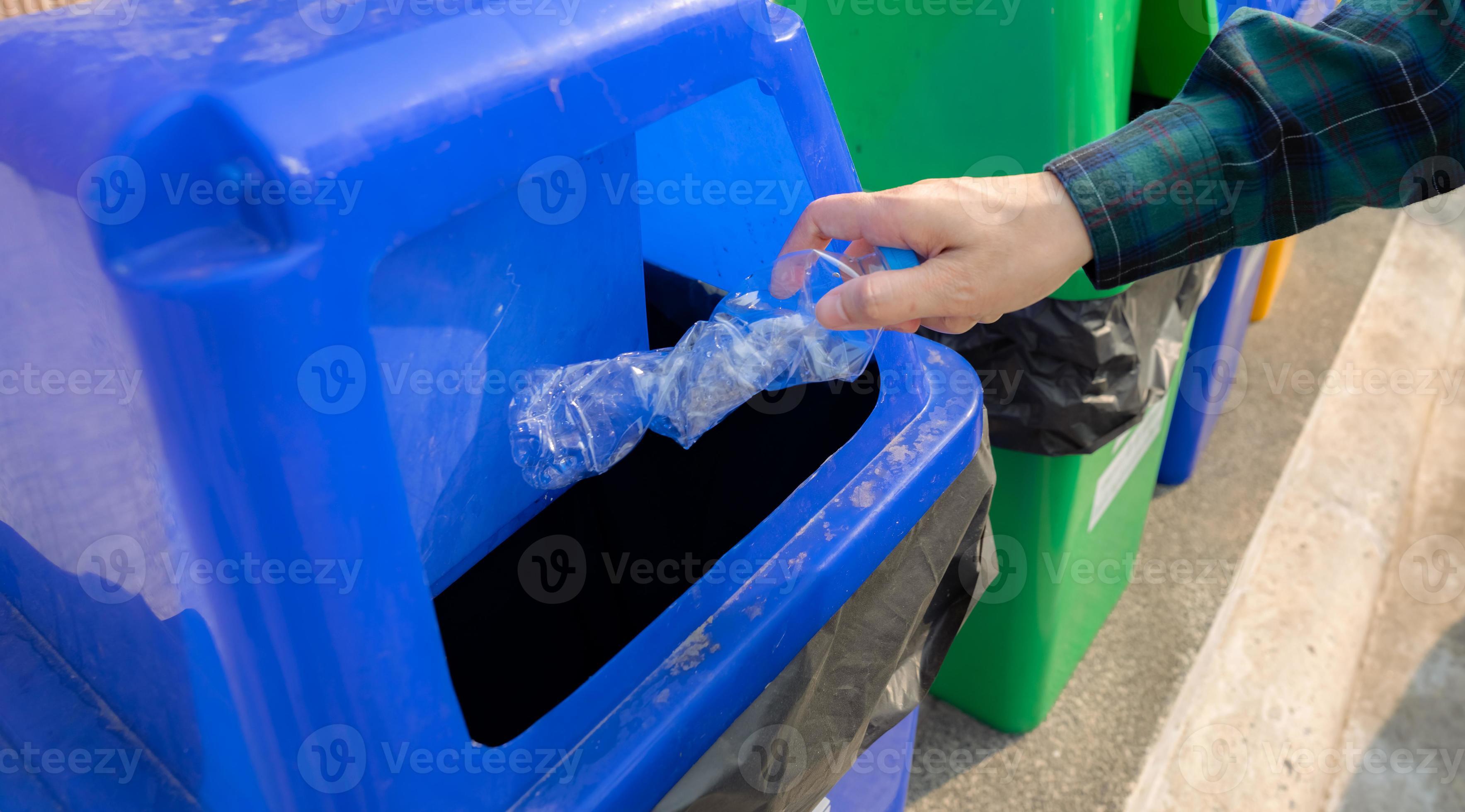 People hand throwing empty water bottle in recycle bin. Blue plastic