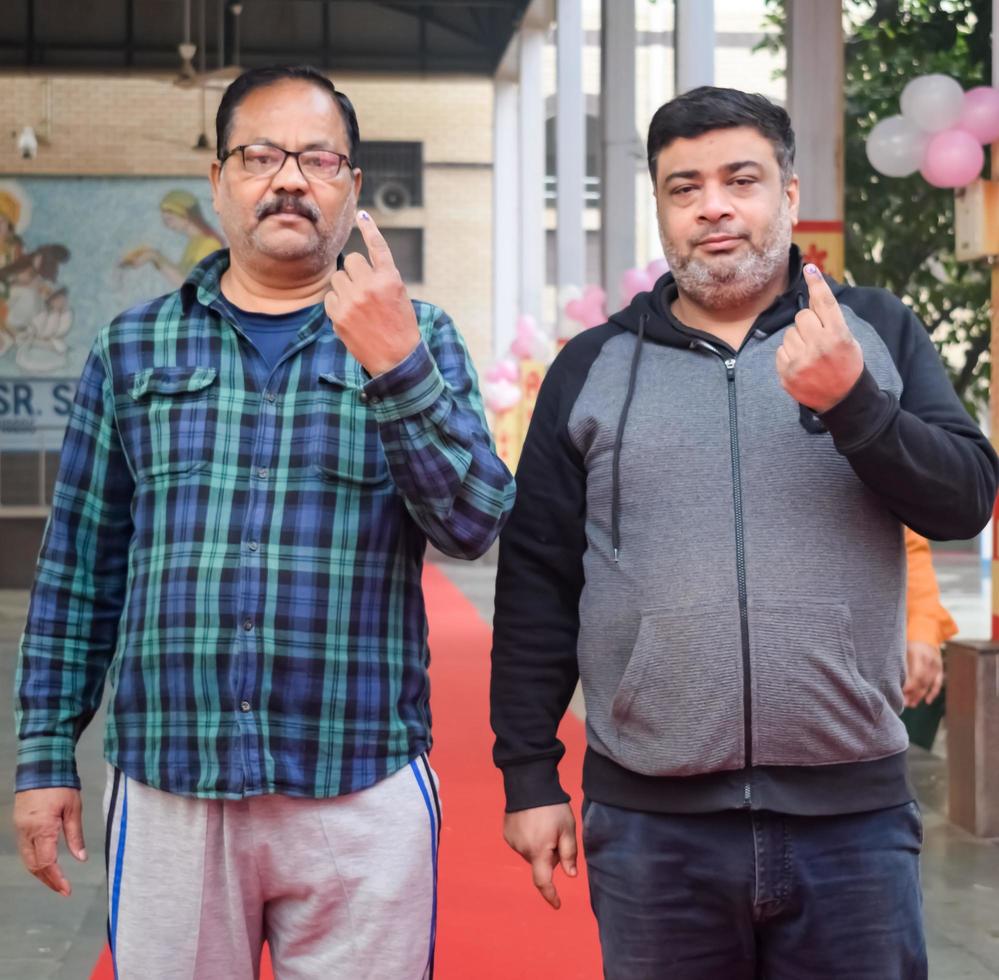 New Delhi, India - December 04 2022 - Unidentified people showing their ink-marked fingers after casting votes in front of polling booth of east Delhi area for MCD local body Elections 2022 photo