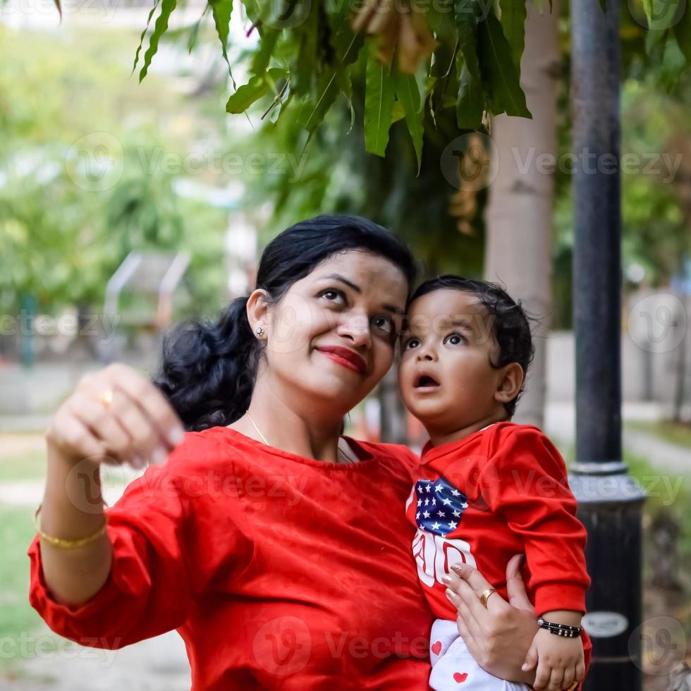 amoroso mamá que lleva de su bebé a sociedad parque. brillante retrato de contento mamá participación niño en su manos. madre abrazando su pequeño 9 9 meses antiguo hijo. foto