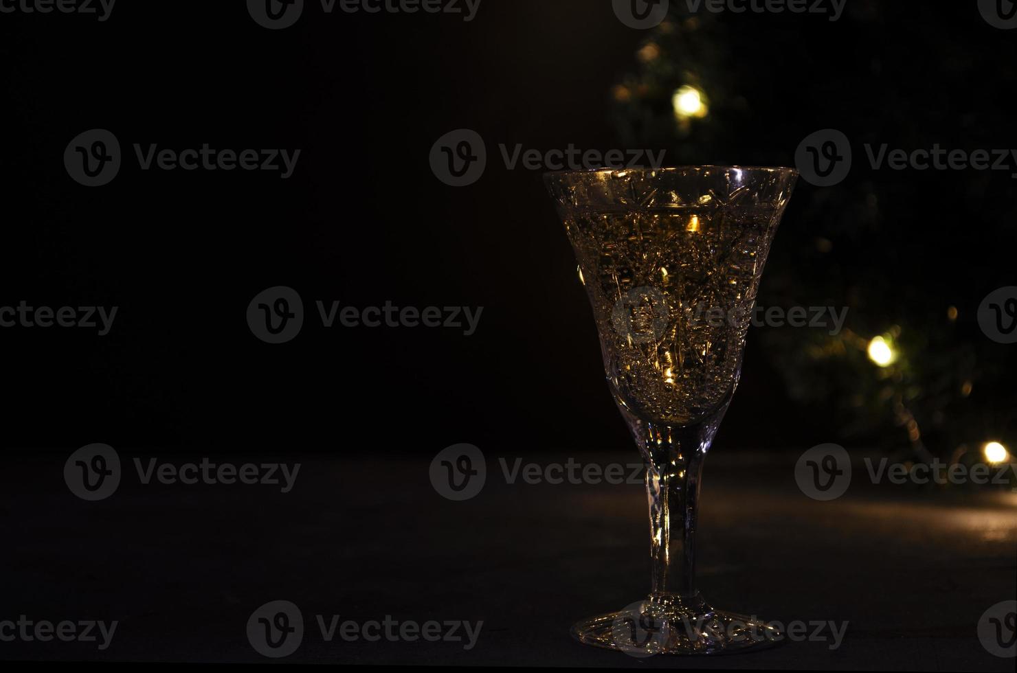 Glass with white wine with garland lights on the background. dark picture. Golden beverage in the glass. Beautiful lights reflected in the glass. photo