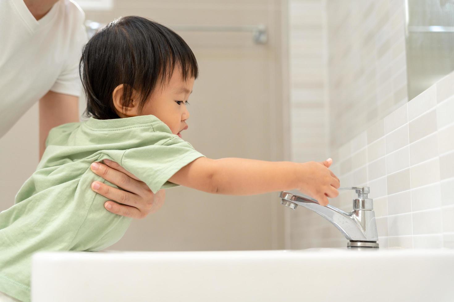 pequeño niño mano cerrado el grifo a lavabo en casa con mamá. madre enseña niño a salvar agua. mantiene torneado apagado el agua a salvar mundo energía y proteger el ambiente, mundo agua día foto