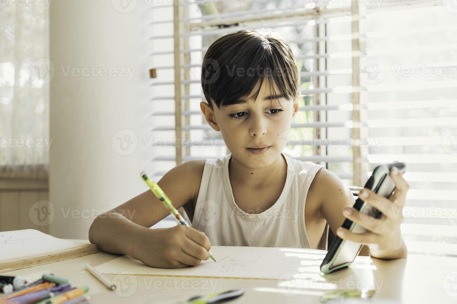 Child drawing in a bright home copying an image from a cell phone. Concept of creativity, technology and learning. photo