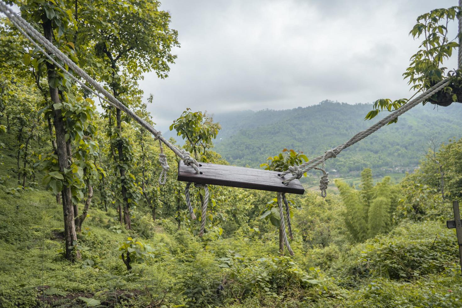 Landscape of empty swinging on the middle tropical forest with green hill view. The photo is suitable to use for nature background, holiday content social media and hill view poster.