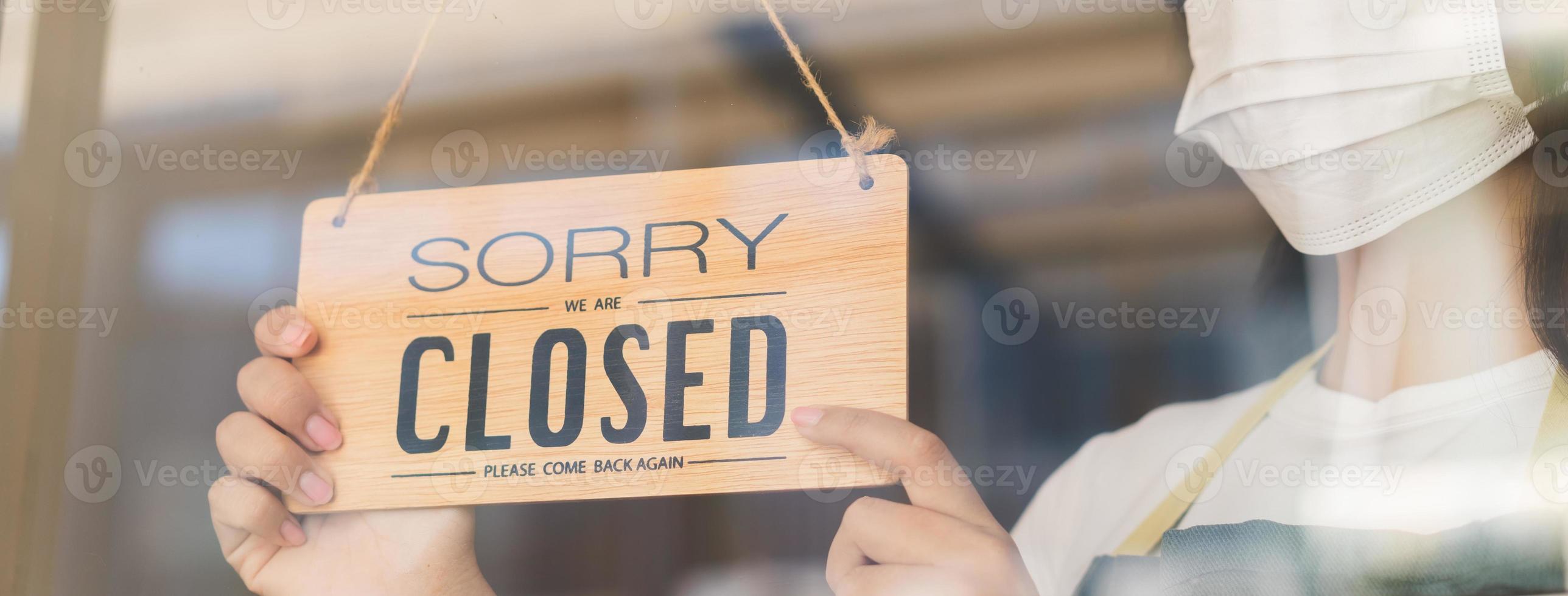 Asian young owner retail,coffee shop woman turning sign board to closed with wearing face mask,protection to pandemic of coronavirus.Close store,restaurant or pub due to lockdown, quarantine of covid. photo