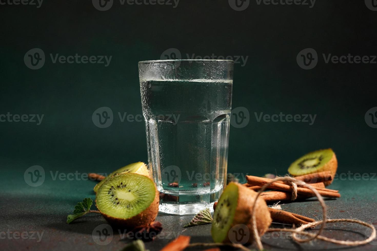 A Glass of Cold Water on a Green background. Decorated with slice kiwi, cinnamon sticks, badyan, mint leaves. Copy space photo