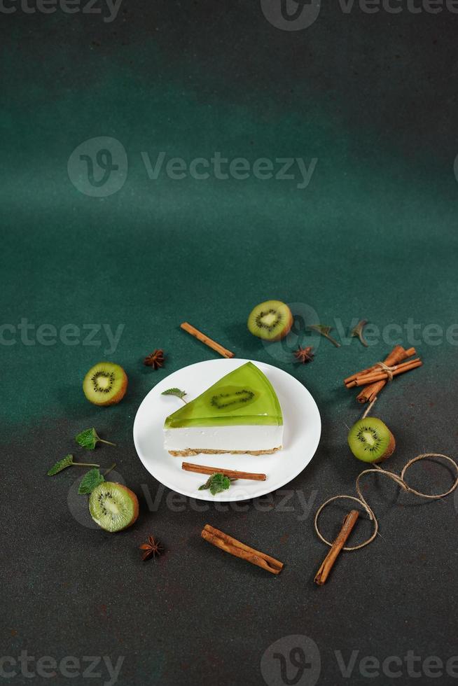 Cheesecake with Kiwi, cinnamon stick and leaves mint on a green background. Copy cpase for text photo