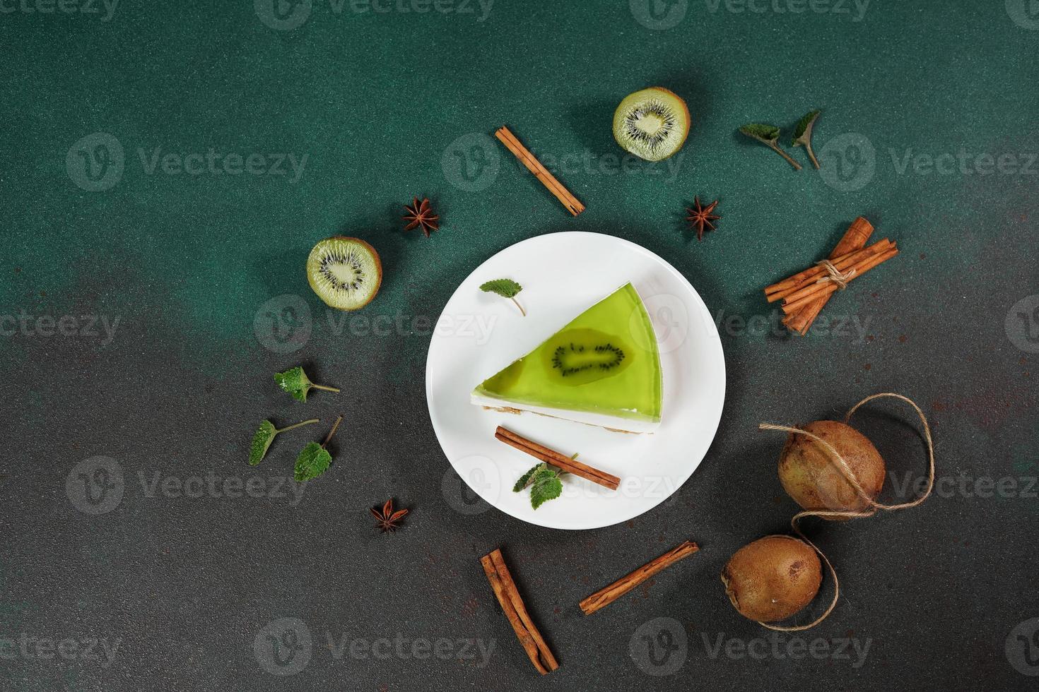 Homemade Cheesecake with Kiwi in a white plate on a Green background. Decoreted with slice of kiwi, cinnamon stick and leaves mint. Top view photo