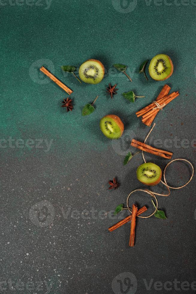 Slices of fresh, juicy Kiwi on a Green background. Decorated with cinnamon sticks, badyan, mint leaves. Fruity decorated background. Top view photo