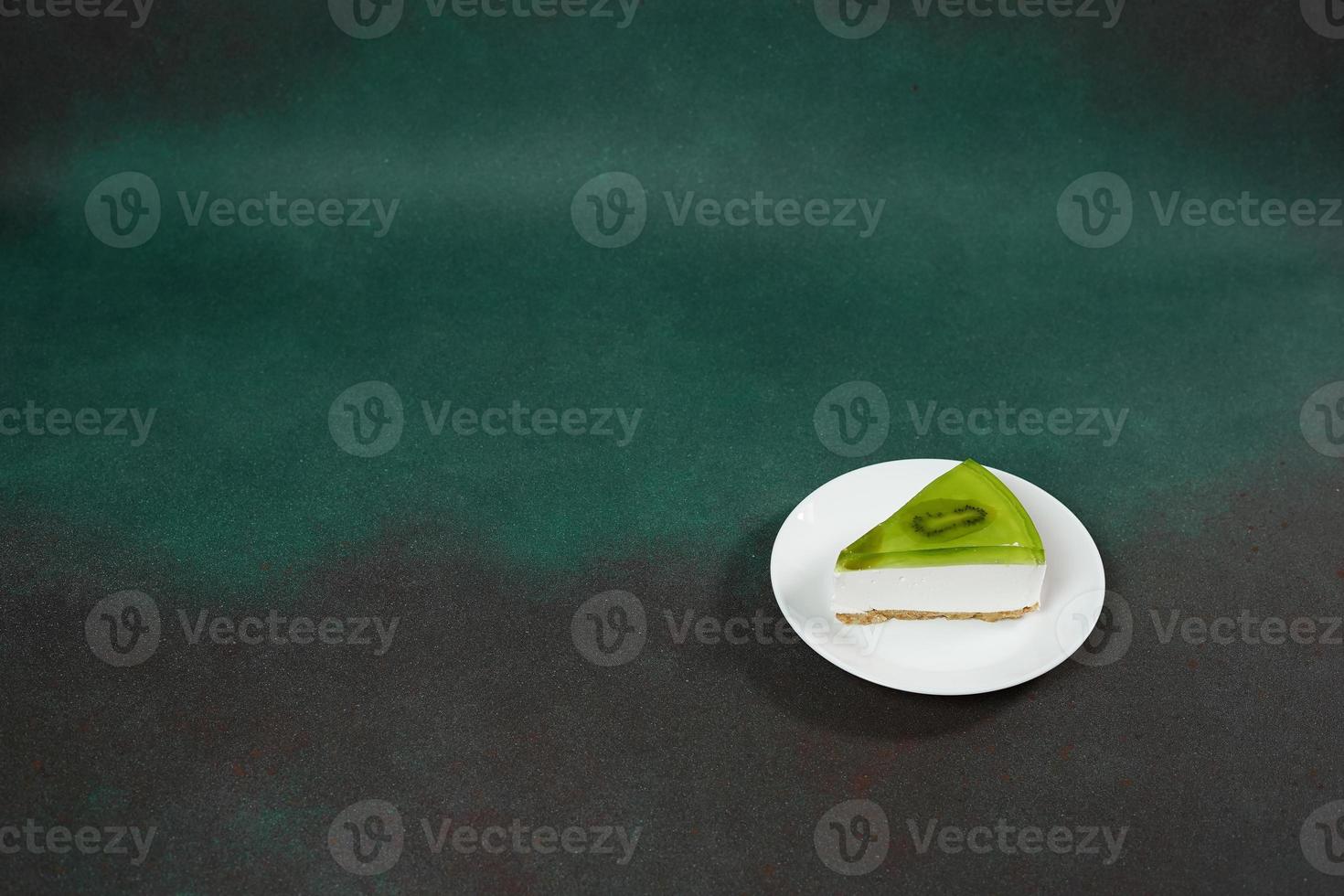 Slice of Cheesecake with Kiwi, cinnamon stick and leaves mint on a green background. Copy cpase for text photo