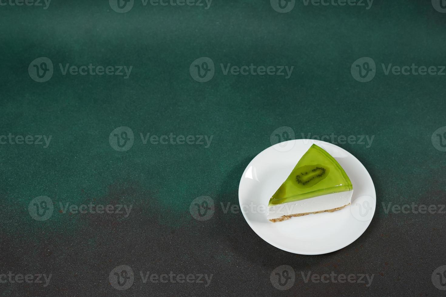 Slice of Cheesecake with Kiwi, cinnamon stick and leaves mint on a green background. Copy cpase for text photo