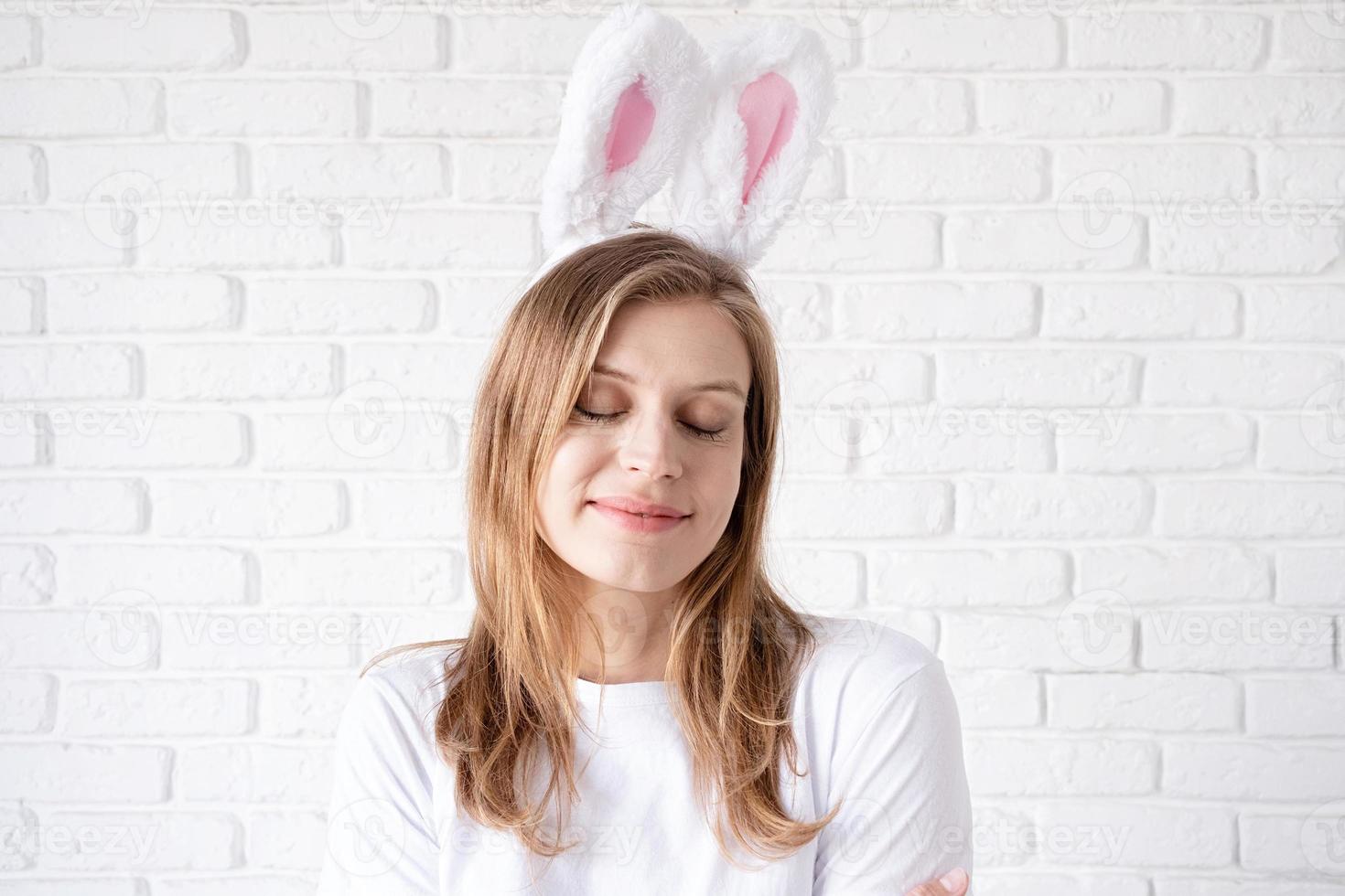 Portrait of a happy woman in bunny ears on white brick wall background photo