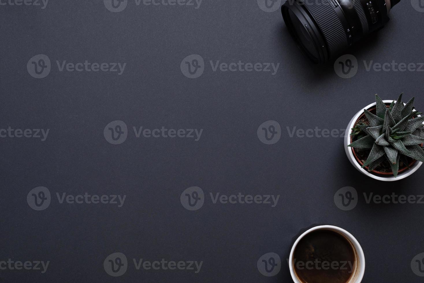 Photographer work desk composition with camera lens, plant and coffe mug. Top view, flat lay with copy space on black desk photo