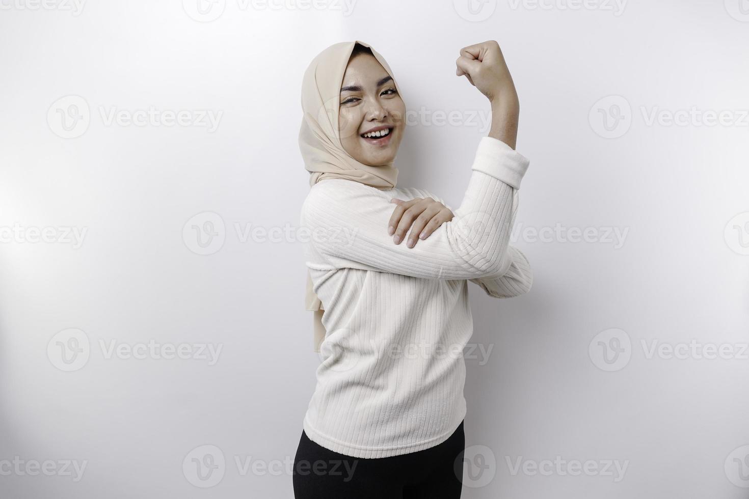 Excited Asian Muslim woman wearing a headscarf showing strong gesture by lifting her arms and muscles smiling proudly photo