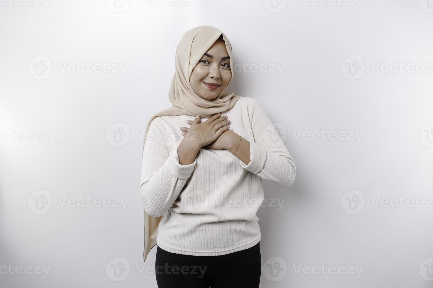 Happy mindful thankful young Asian Muslim woman with her hand on her chest smiling isolated on white background photo