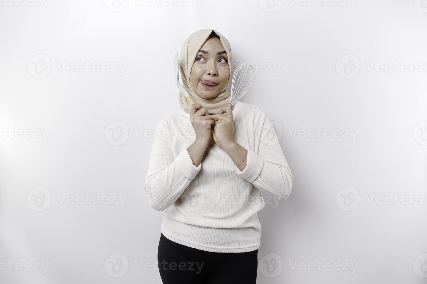 Excited Asian Muslim woman wearing a headscarf, holding cooking ware and smiling, isolated by white background photo