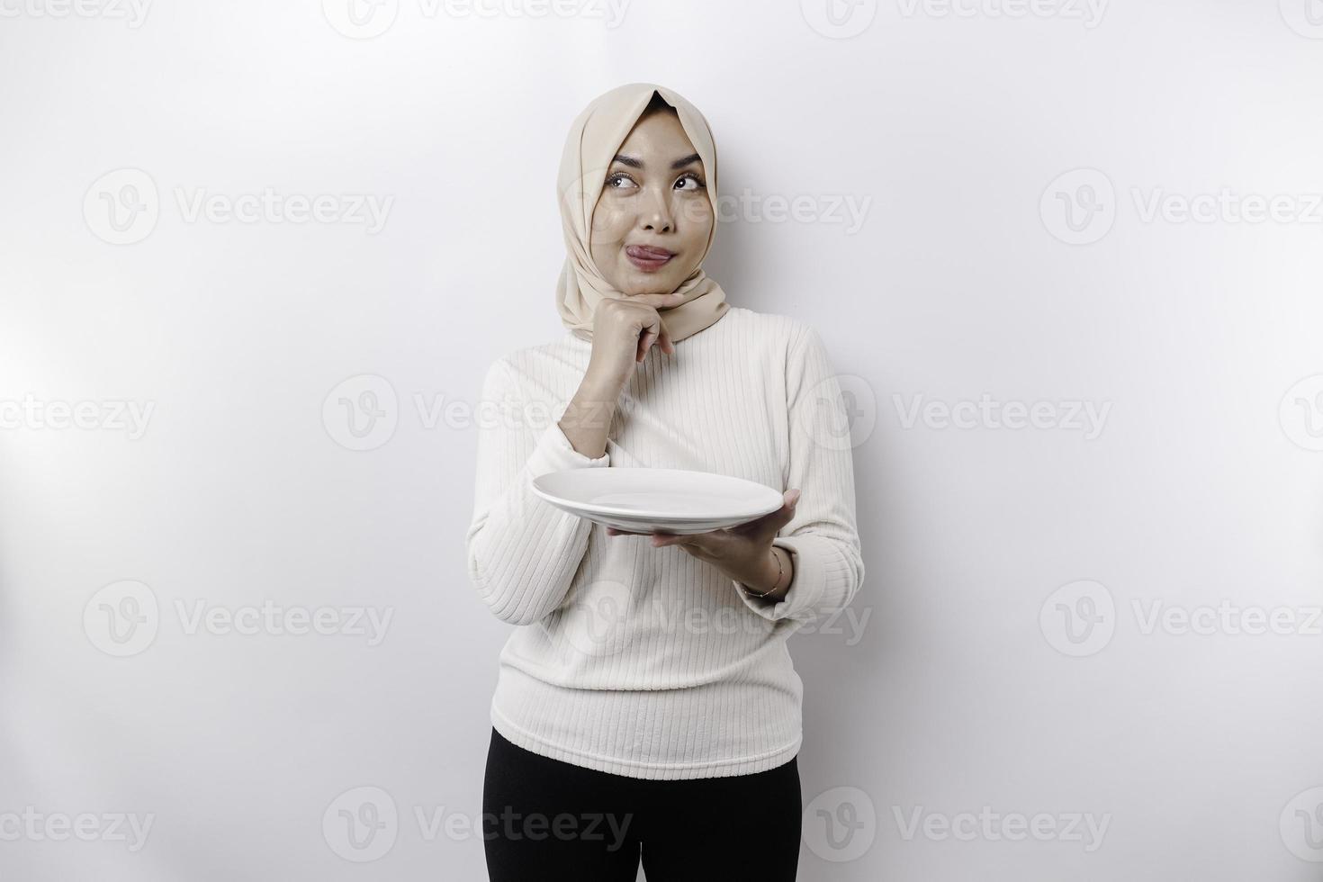 un asiático musulmán mujer es rápido y hambriento y participación un plato mientras mirando aparte pensando acerca de qué a comer foto