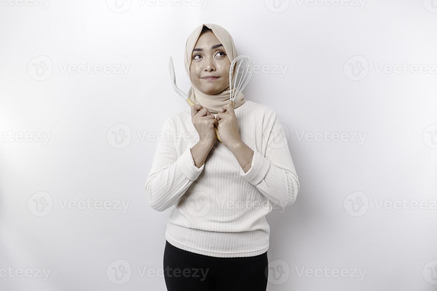 emocionado asiático musulmán mujer vistiendo un Pañuelo, participación Cocinando mercancía y sonriente, aislado por blanco antecedentes foto