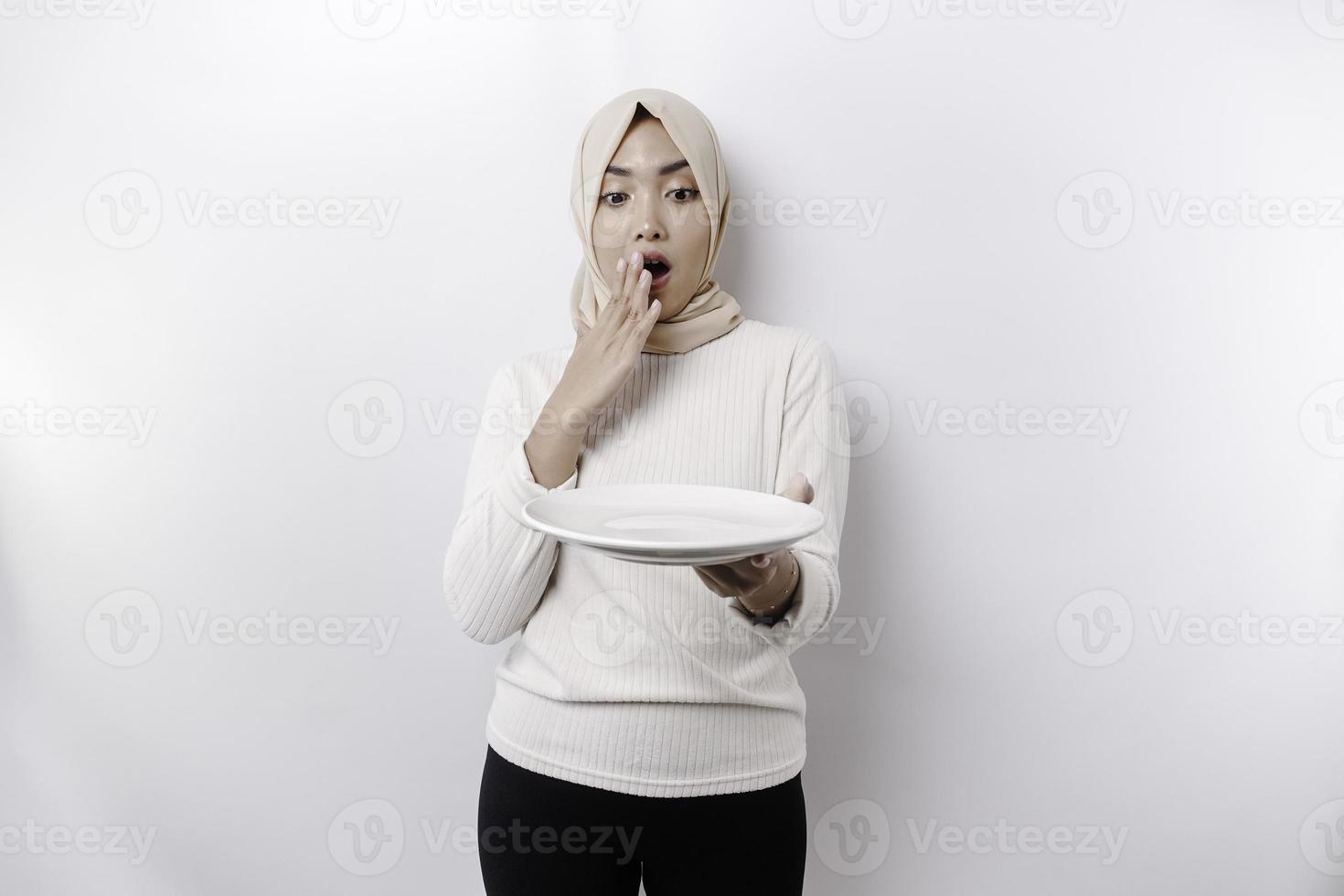 un conmocionado asiático musulmán mujer es rápido y hambriento y participación un plato con su boca amplio abierto foto