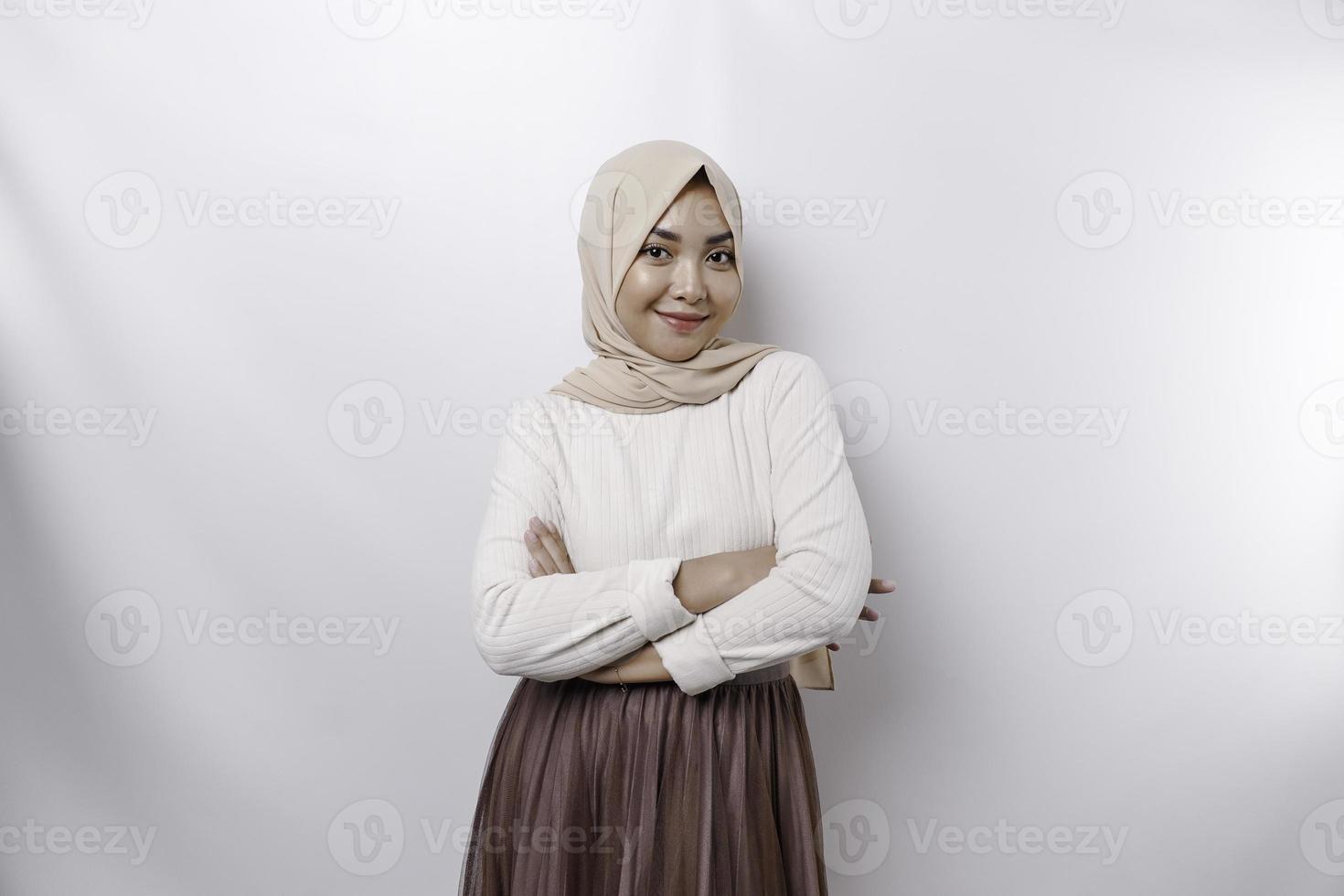 A confident smiling Asian Muslim woman wearing hijab standing with arms folded and looking at the camera isolated over white background photo