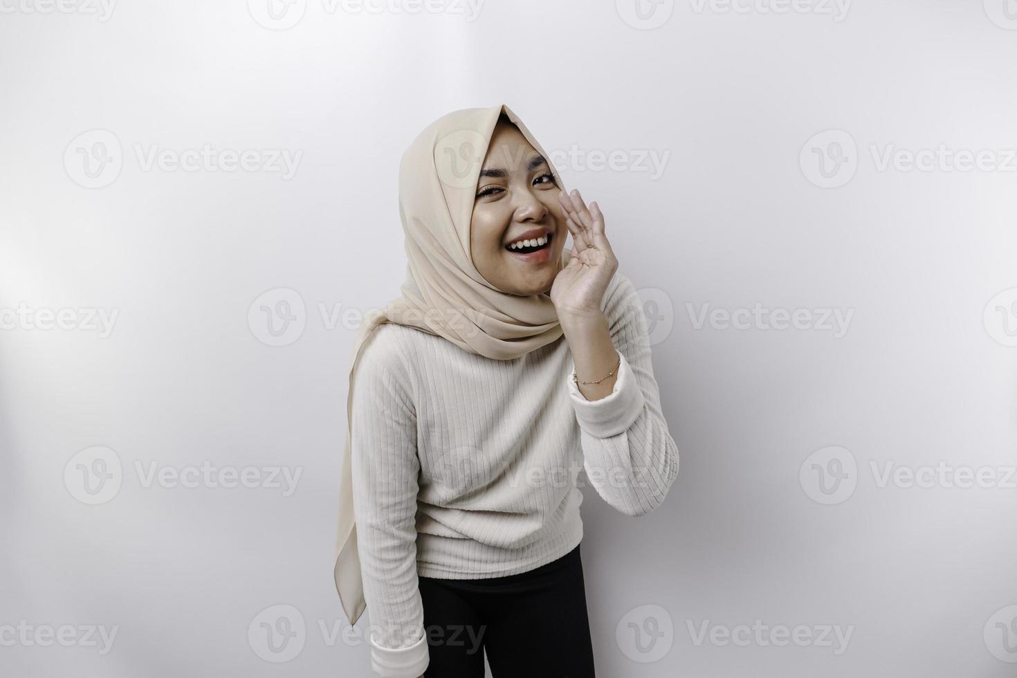 Young beautiful Asian Muslim woman wearing a headscarf shouting and screaming loud with a hand on her mouth. communication concept. photo