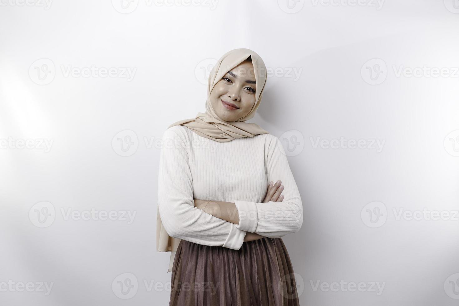 A confident smiling Asian Muslim woman wearing hijab standing with arms folded and looking at the camera isolated over white background photo