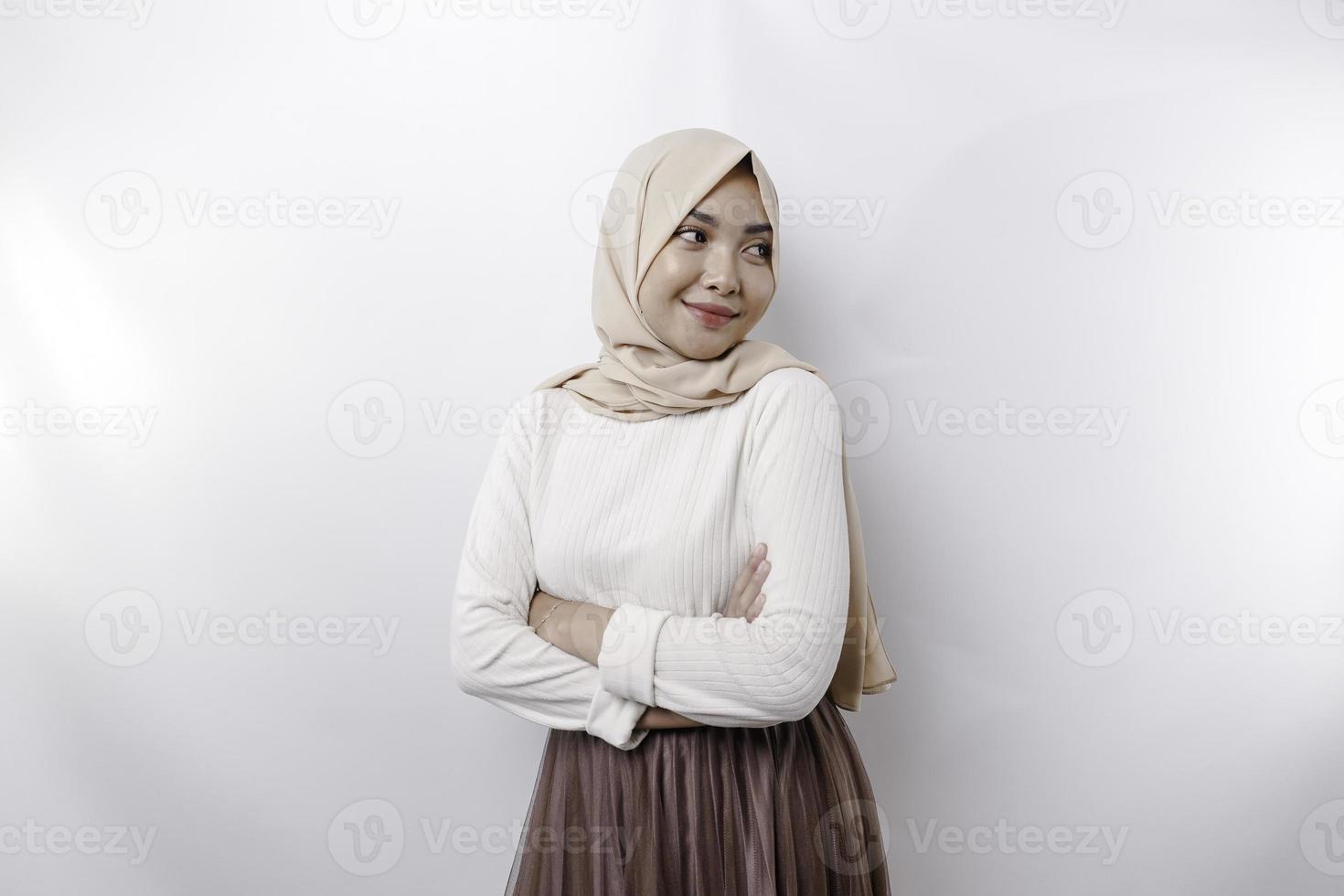 A confident smiling Asian Muslim woman wearing hijab standing with arms folded and looking at the camera isolated over white background photo