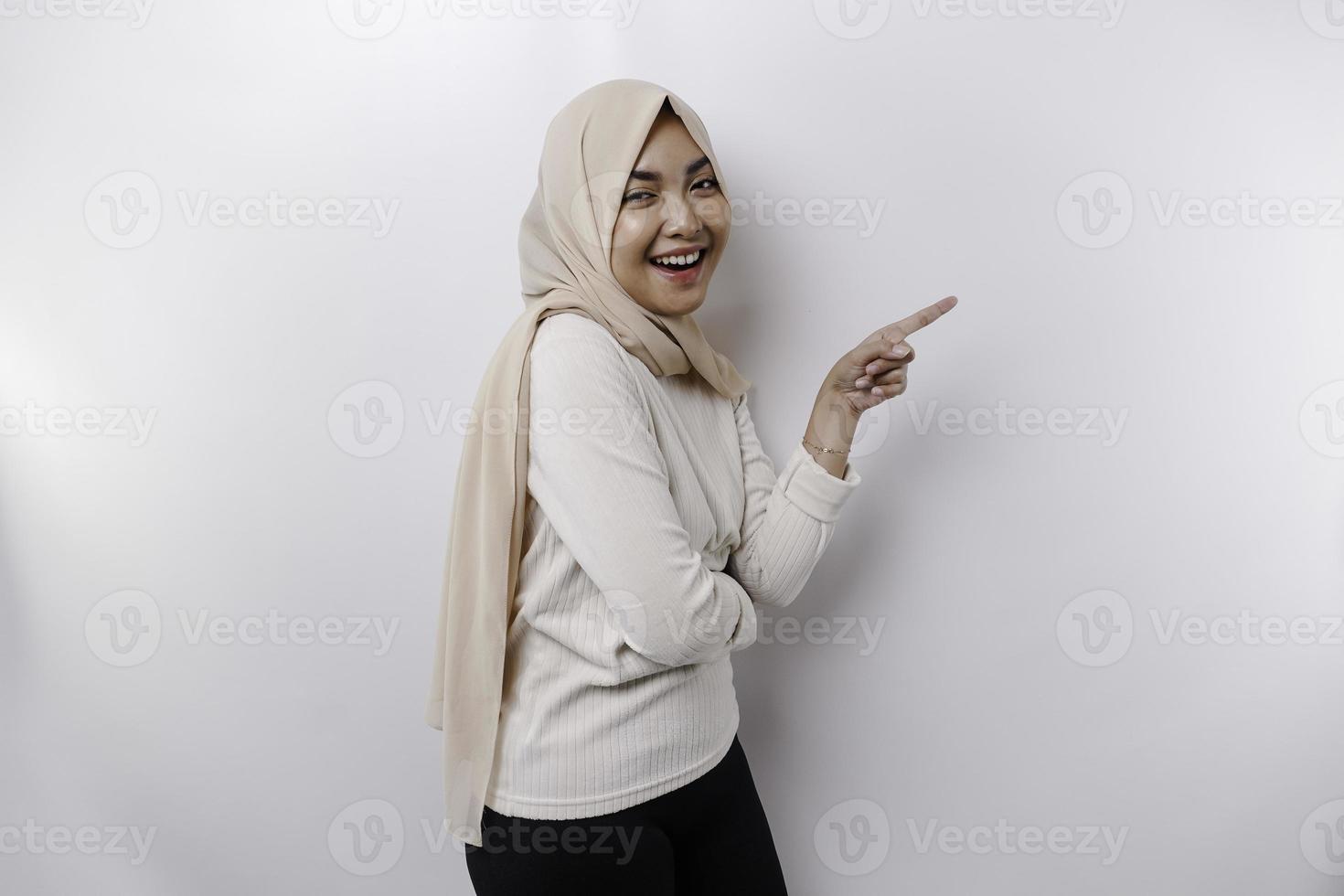 Young Asian Muslim woman smiling while pointing to copy space beside her photo