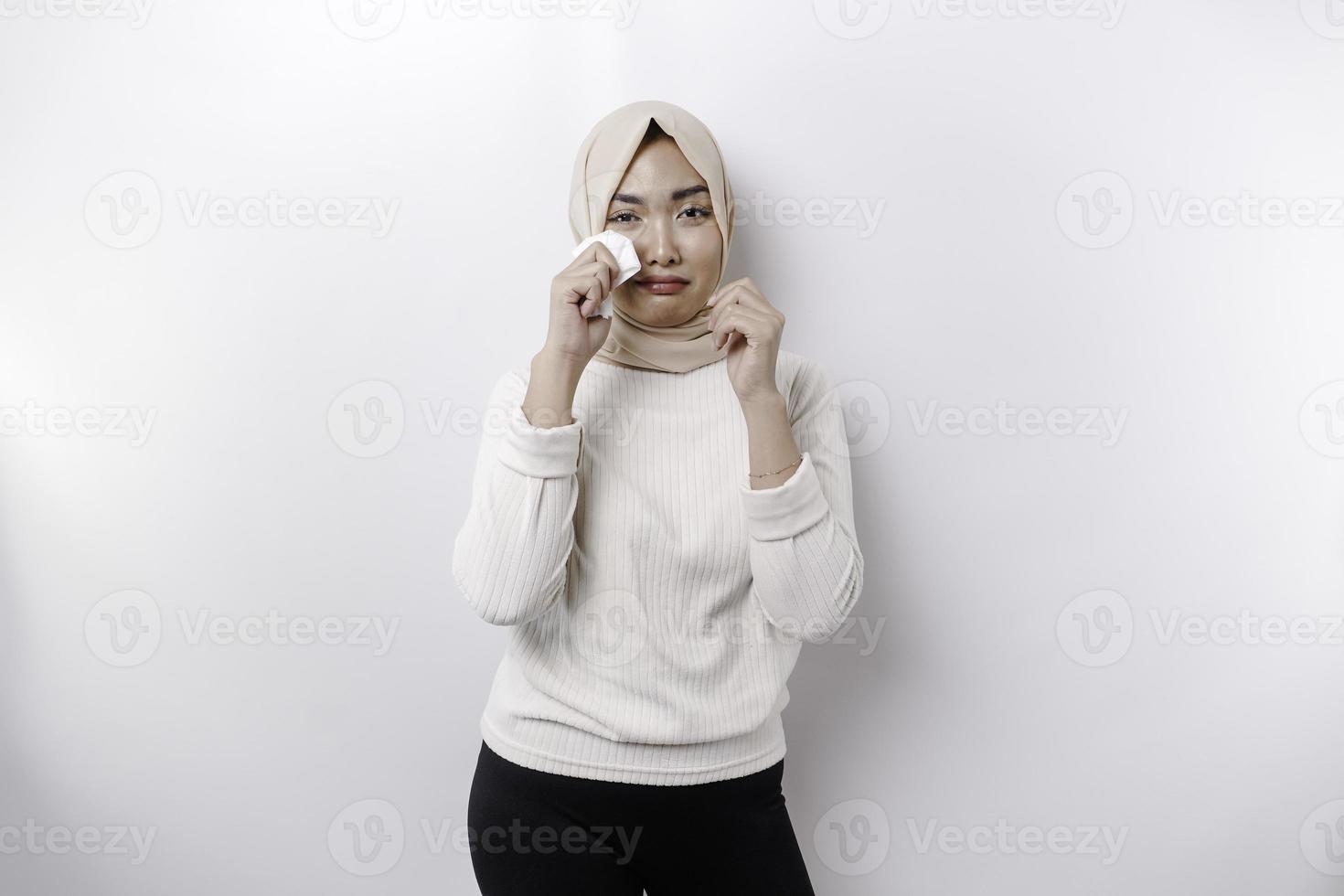 An unhappy Asian Muslim woman wearing a headscarf is wiping her tears in despair, feeling depressed and lonely. photo