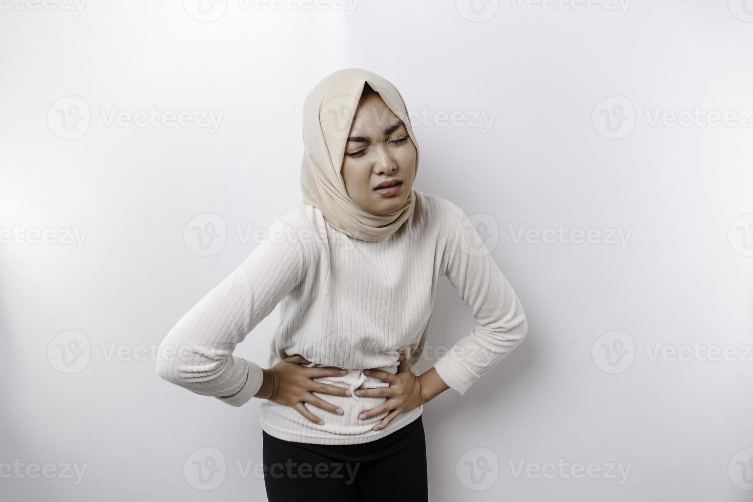 An Asian Muslim woman is fasting and hungry and touching her belly while looking aside thinking about what to eat photo