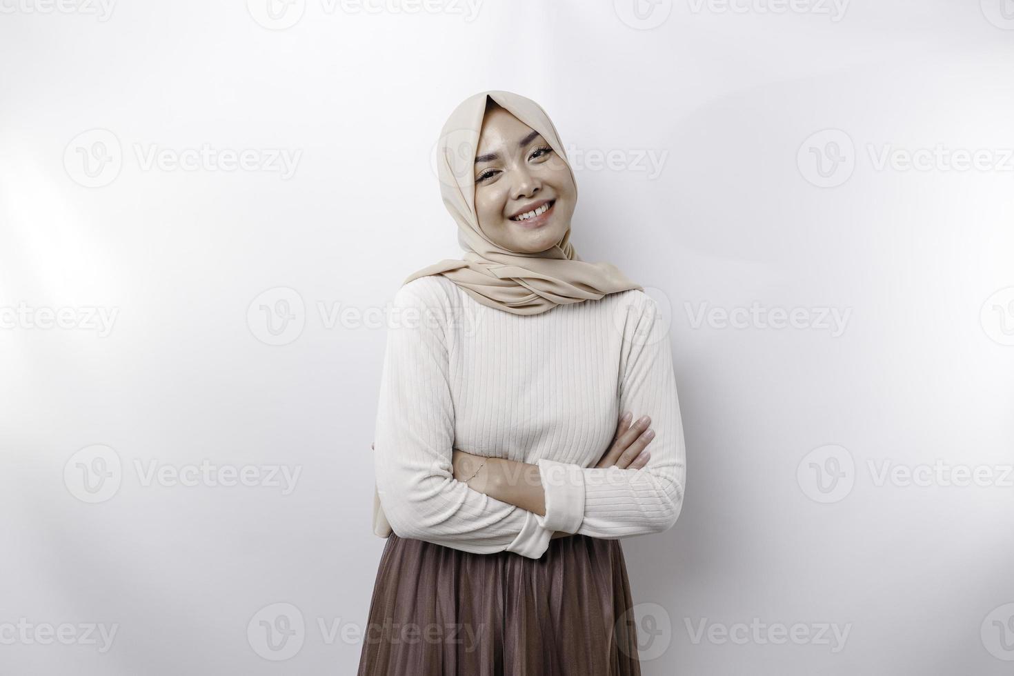 A confident smiling Asian Muslim woman wearing hijab standing with arms folded and looking at the camera isolated over white background photo