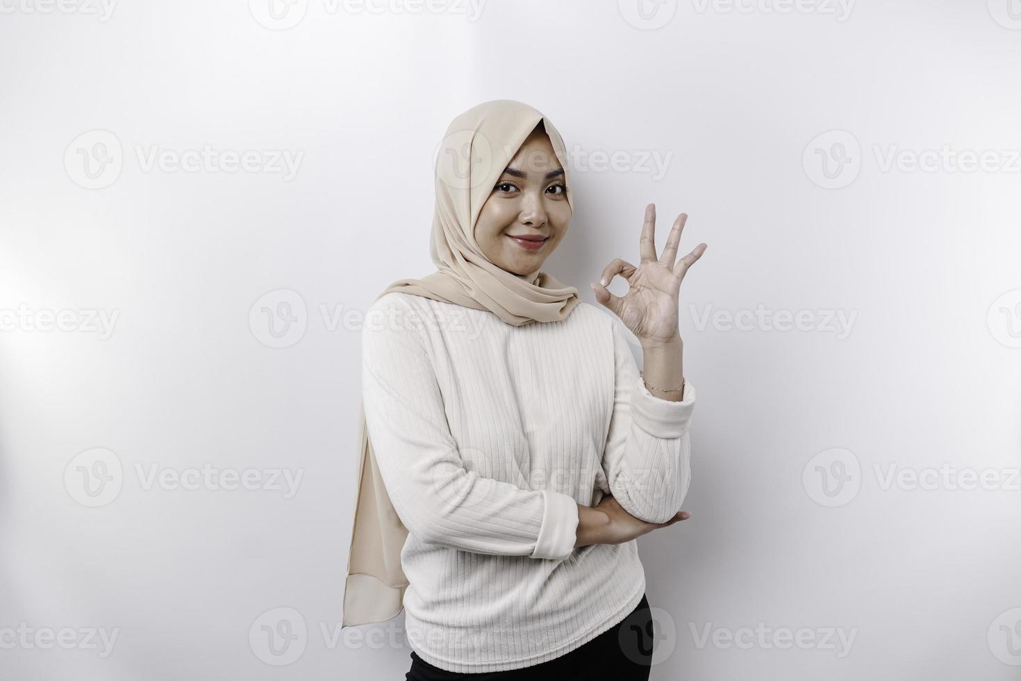 A smiling Asian Muslim woman, giving an OK hand gesture isolated over white background photo