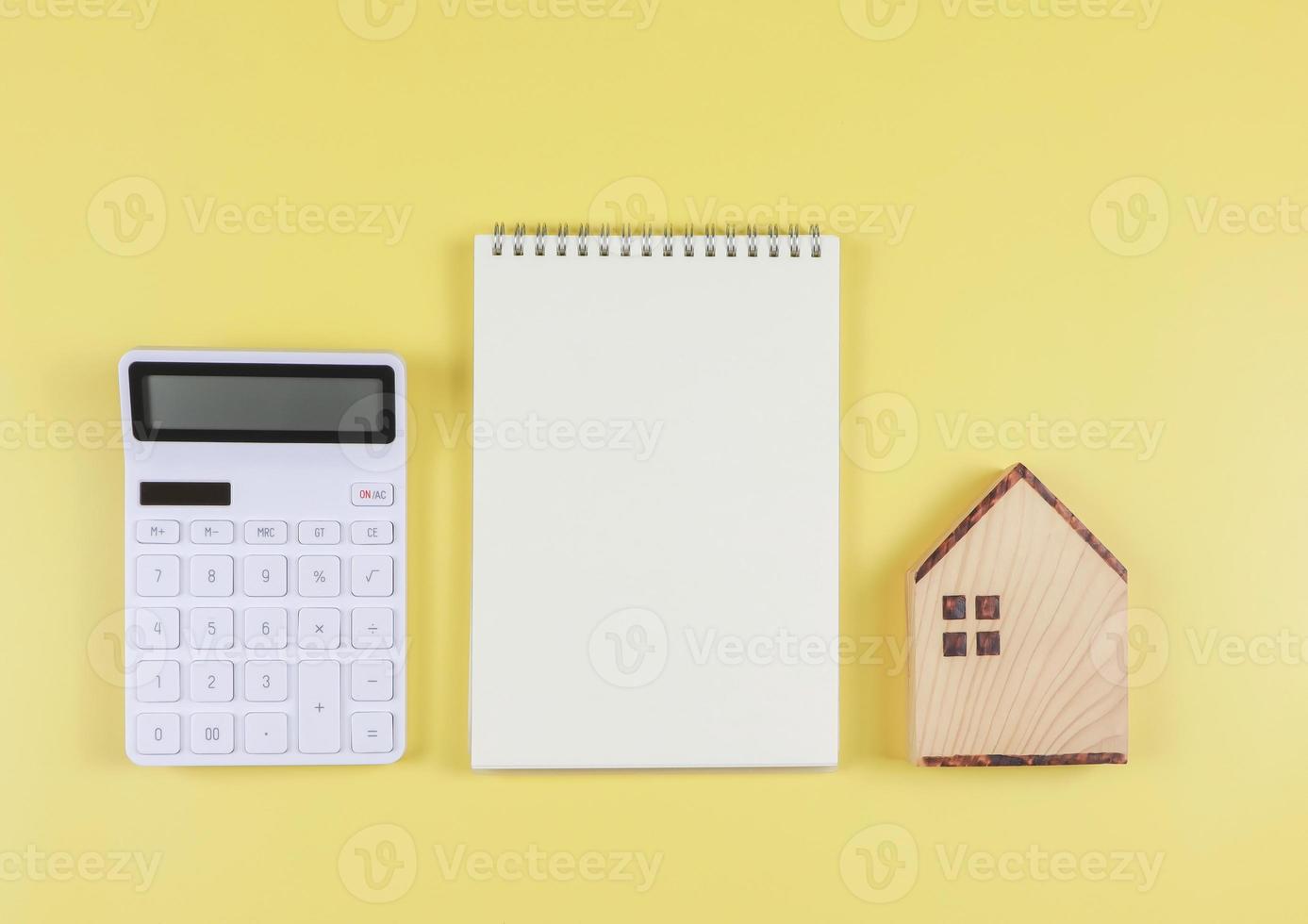 flat layout of wooden house model, white calculator, blank page opened  notebook  on yellow  background with copy space, home purchase concept. photo