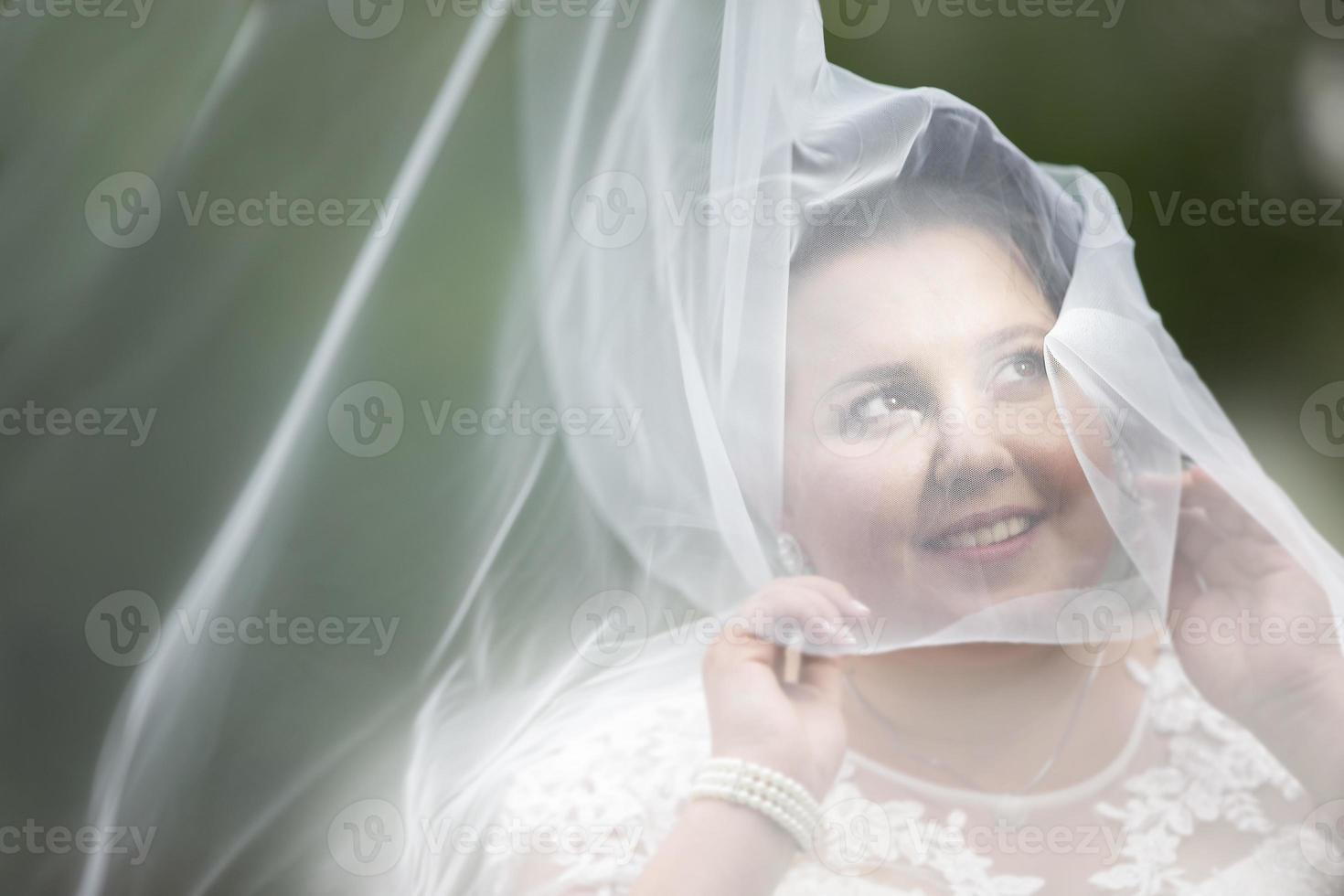 The fat bride hid in a wedding veil against the backdrop of nature. photo