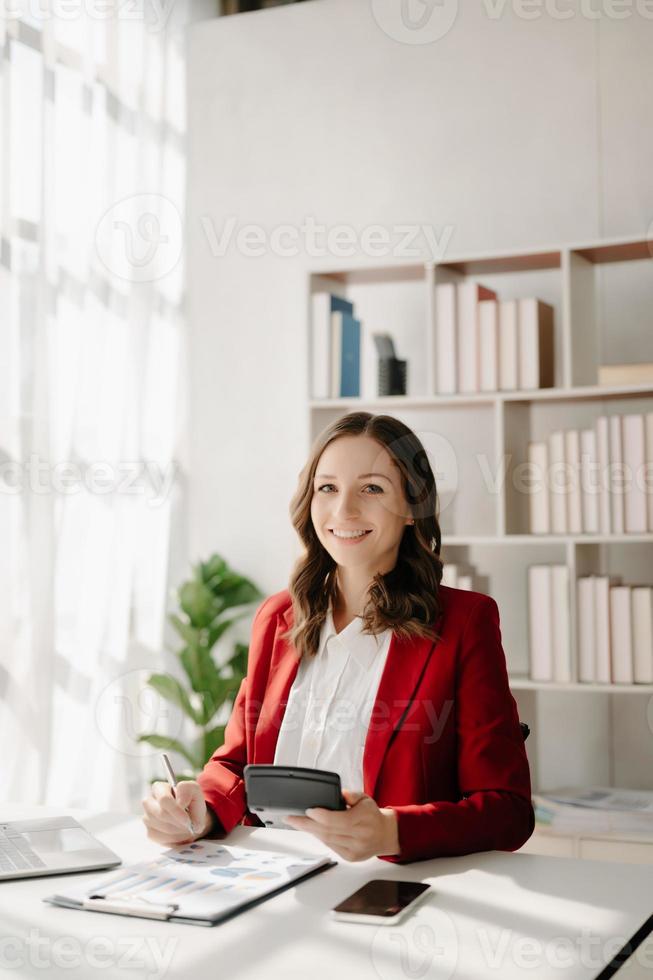 confidente negocio experto atractivo sonriente joven mujer mecanografía ordenador portátil ang participación digital tableta en escritorio en creativo hogar oficina. foto