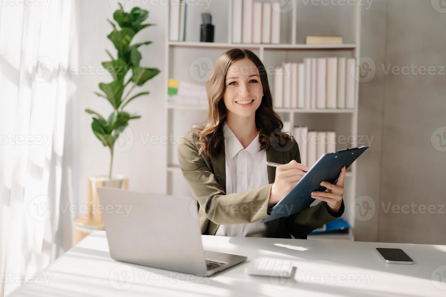 Confident business expert attractive smiling young woman typing laptop ang holding digital tablet  on desk in creative home office. photo