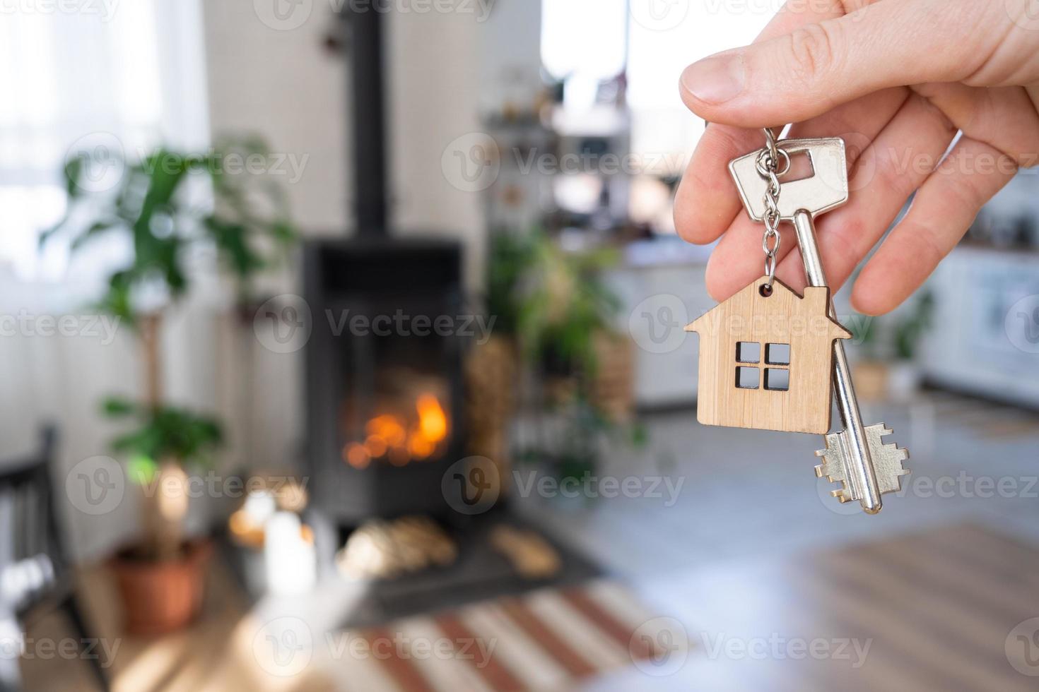 Key to house with keychain against background of fireplace stove with fire and firewood. Cozy home hearth. Building, design, project, moving to new house, mortgage, rent and purchase real estate photo