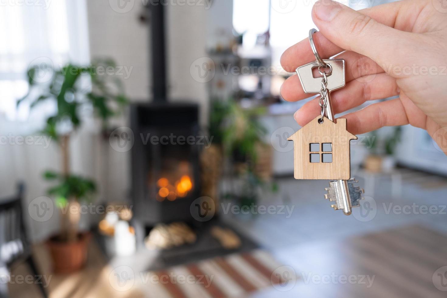 Key to house with keychain against background of fireplace stove with fire and firewood. Cozy home hearth. Building, design, project, moving to new house, mortgage, rent and purchase real estate photo