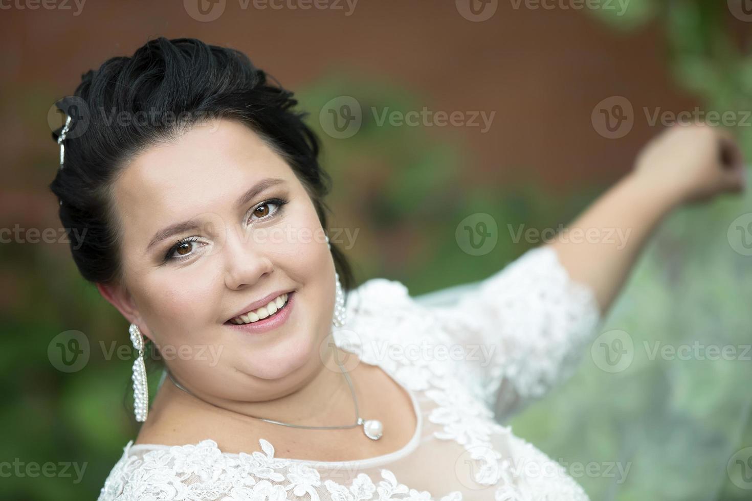 Close-up portrait of a fat bride.Portrait of a plump bride with a waving veil against a background of summer greenery. photo