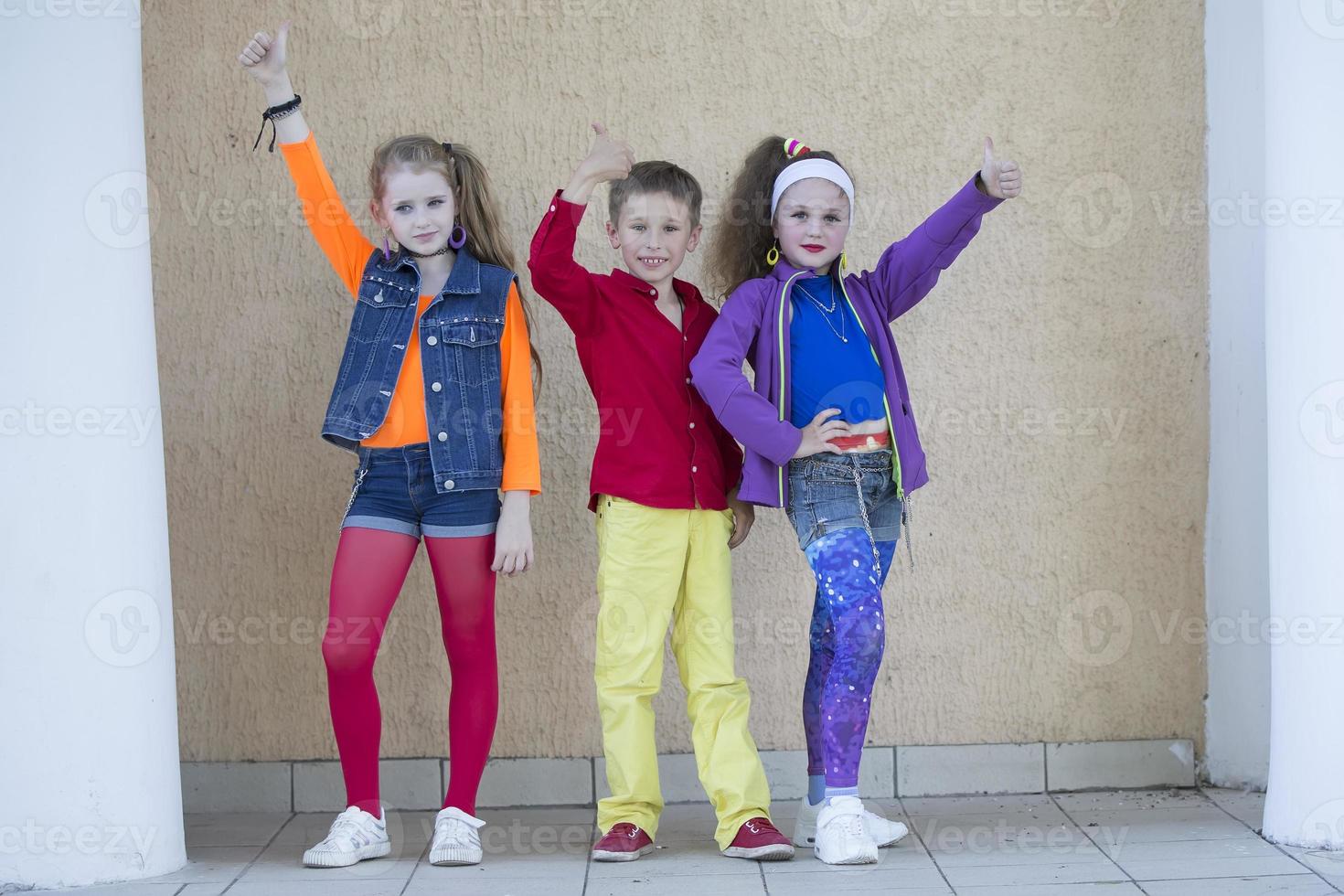 Children pose for a photo shoot. Boy and two little girls models in bright clothes are looking at the camera.