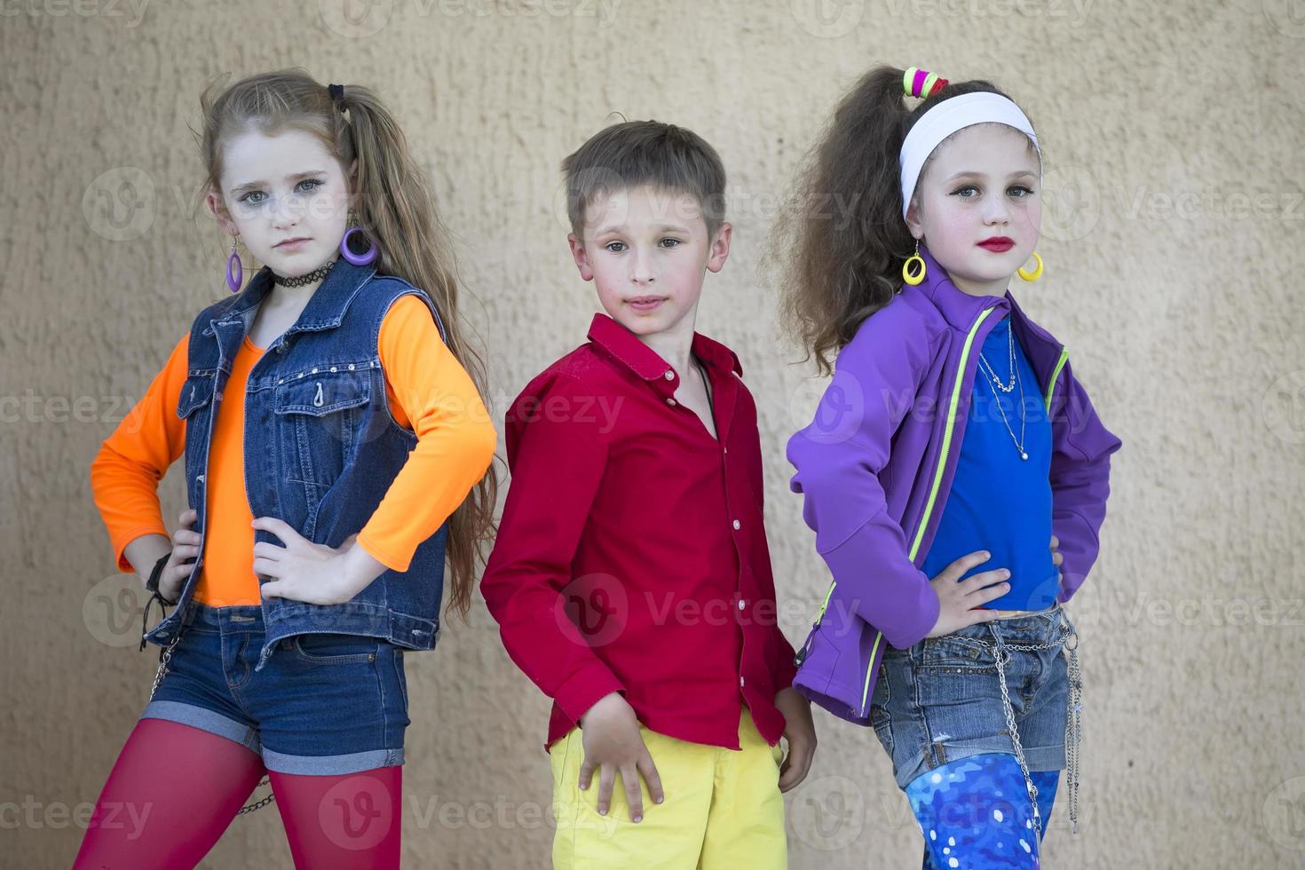 Children pose for a photo shoot. Boy and two little girls models in bright clothes are looking at the camera.