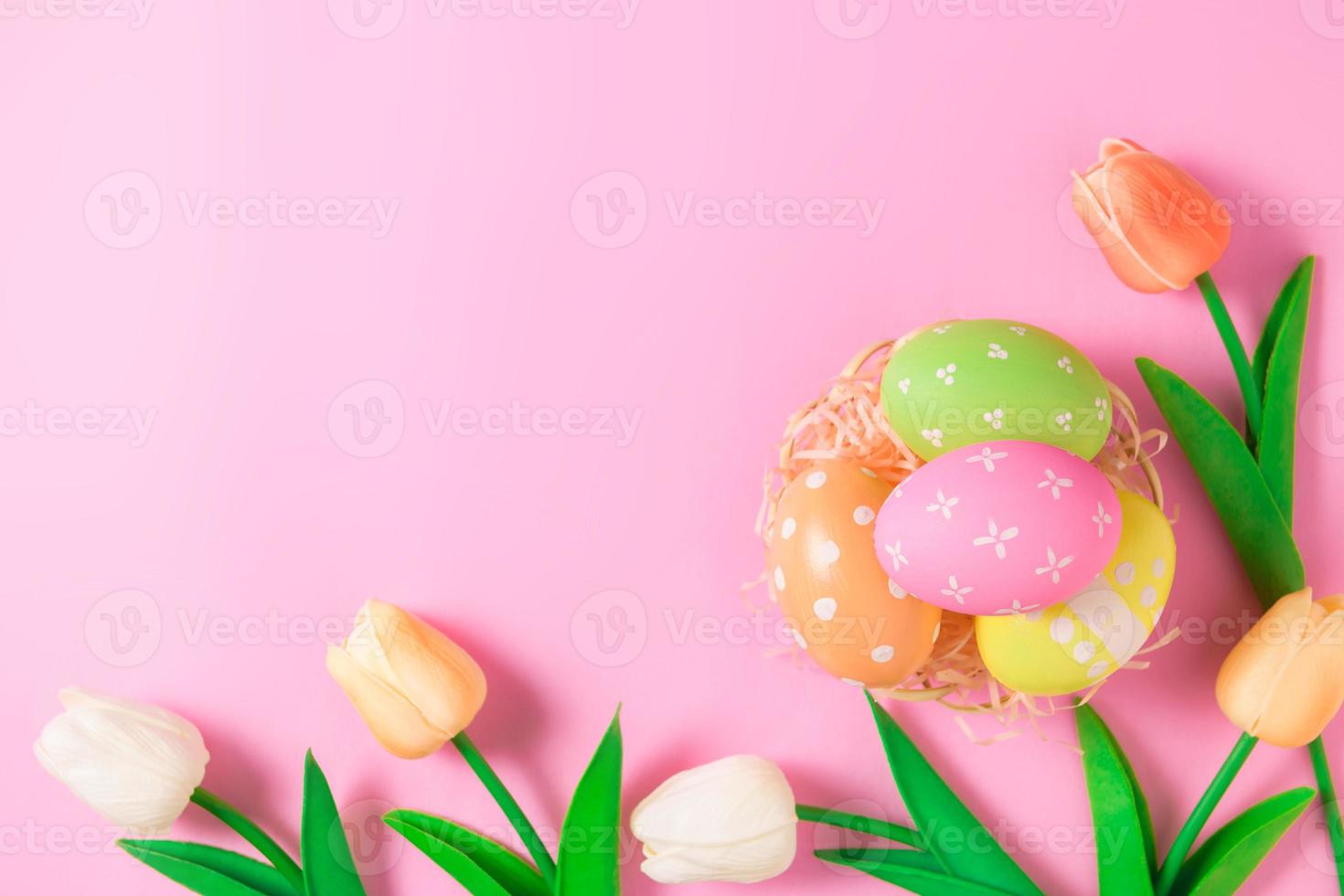 Happy Easter holiday greeting card concept. Colorful Easter Eggs and spring flowers on pastel pink background. Flat lay, top view, copy space. photo