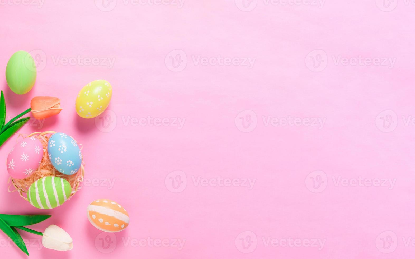 Happy Easter holiday greeting card concept. Colorful Easter Eggs and spring flowers on pastel pink background. Flat lay, top view, copy space. photo