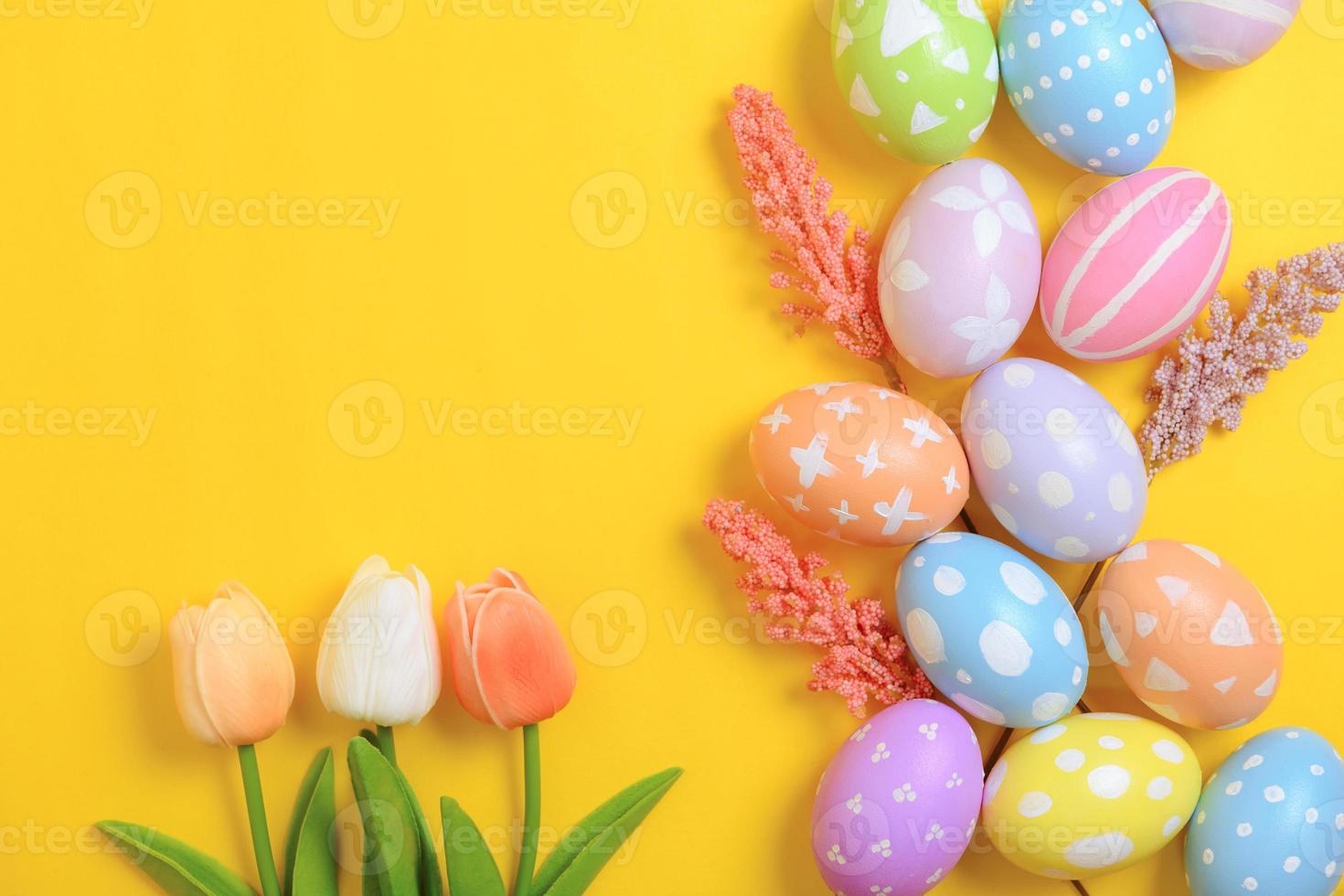 Happy Easter holiday greeting card design concept. Colorful Easter Eggs and spring flowers on yellow background. Flat lay, top view, copy space. photo
